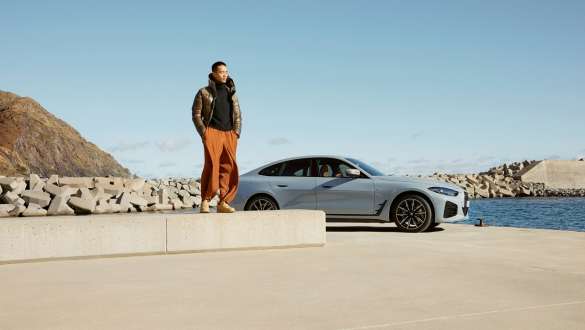 BMW Service Inclusive BMW Service Inclusive ผู้ชายยืนอยู่บนพื้นหินต่างระดับด้านหน้าของรถยนต์ BMW มีน้ำอยู่ด้านหลัง